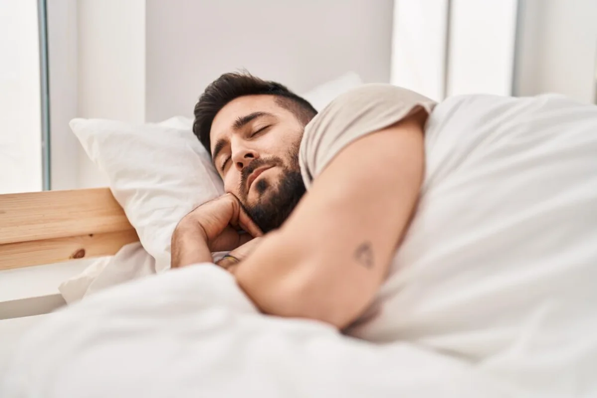 Young man sleeping peacefully in a bright, white bed.