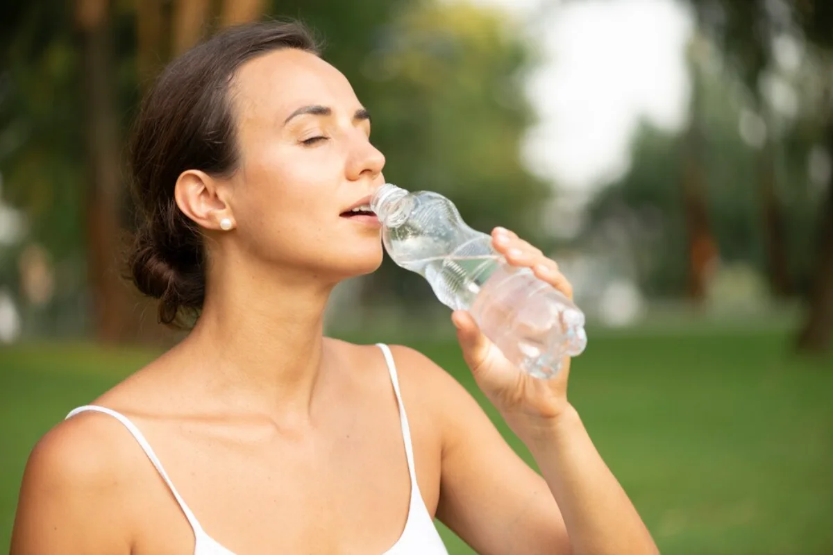 Woman drinking water from a bottle in a park, looking refreshed.