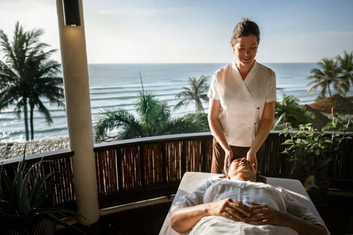 Woman giving a man a head massage on a balcony overlooking a beach.