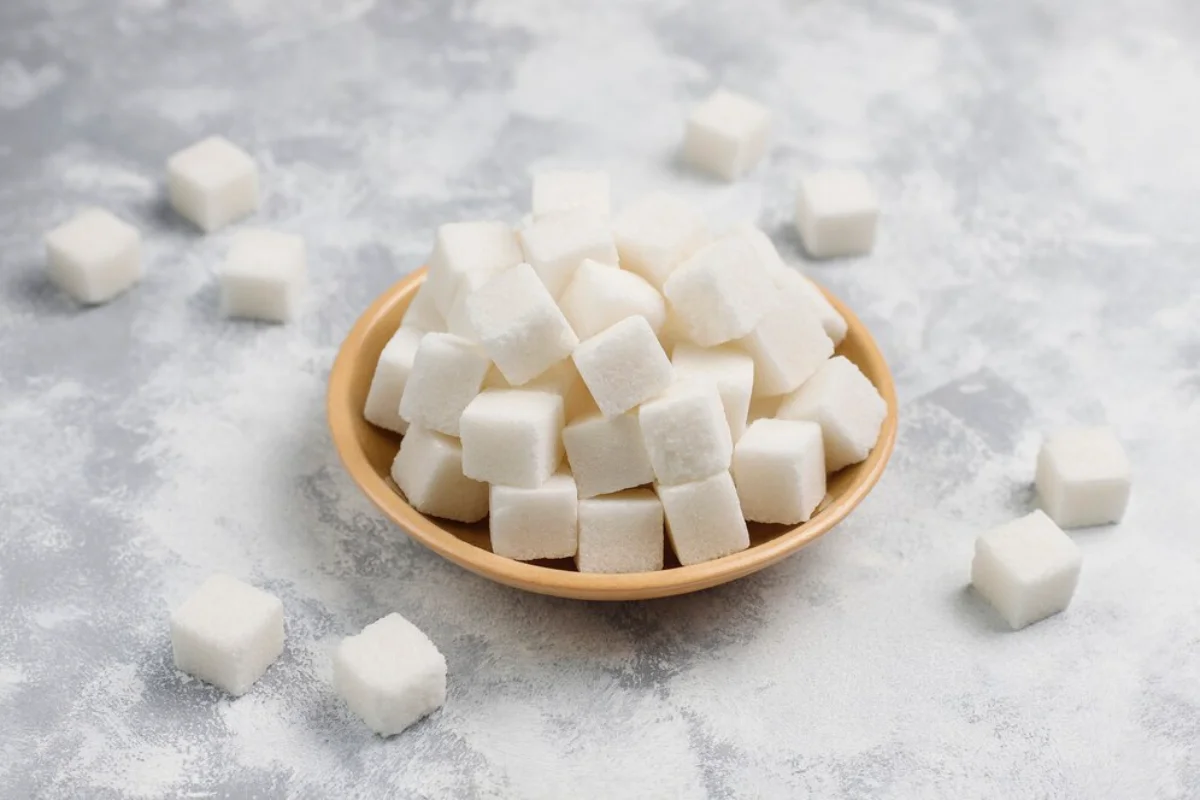 A bowl of white sugar cubes on a textured grey surface.