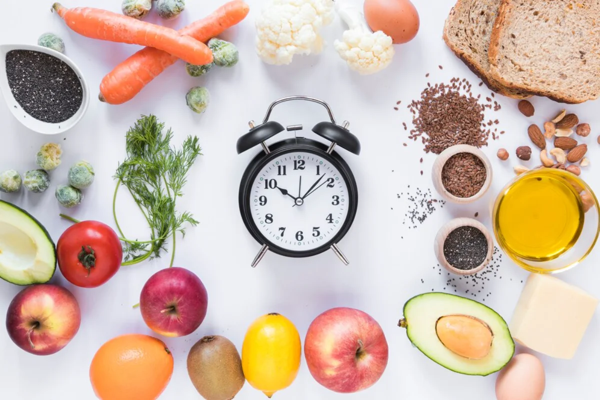 Alarm clock surrounded by various healthy foods including fruits, vegetables, nuts, seeds, and whole grains on a white surface.