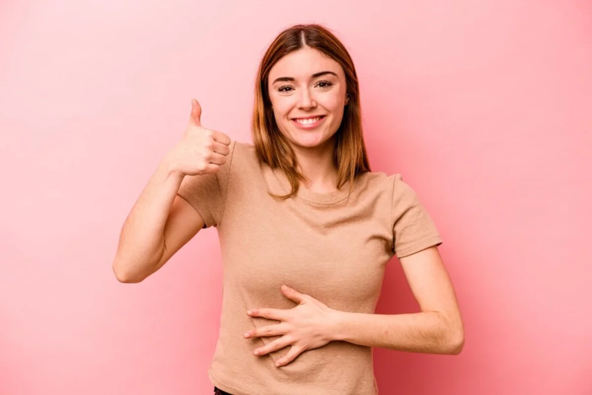 Young woman giving a thumbs up against a pink background.