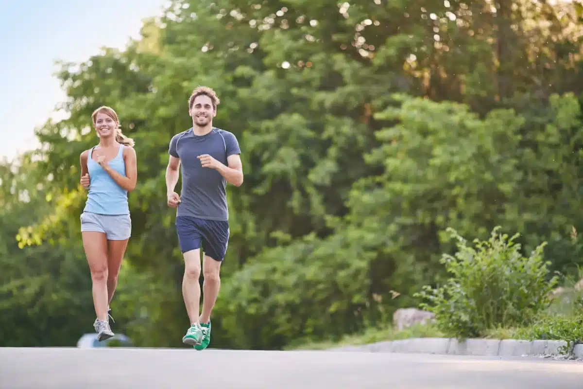 A man and a woman jogging together on a sunny park path.