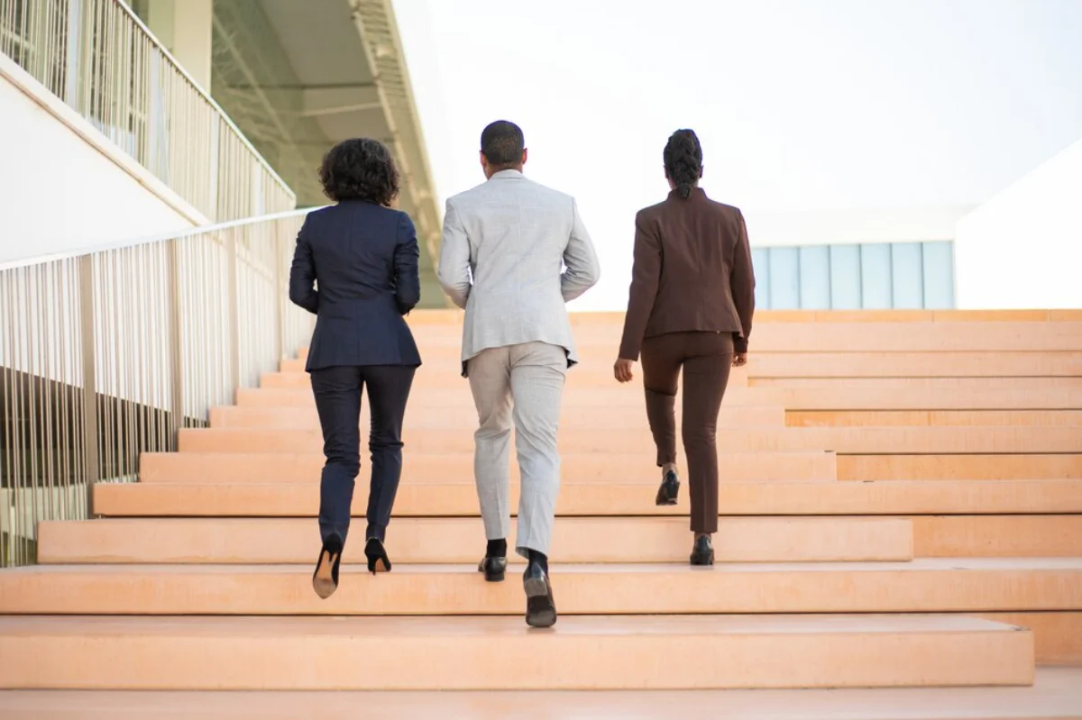 Three professionals in business attire walking up outdoor steps.