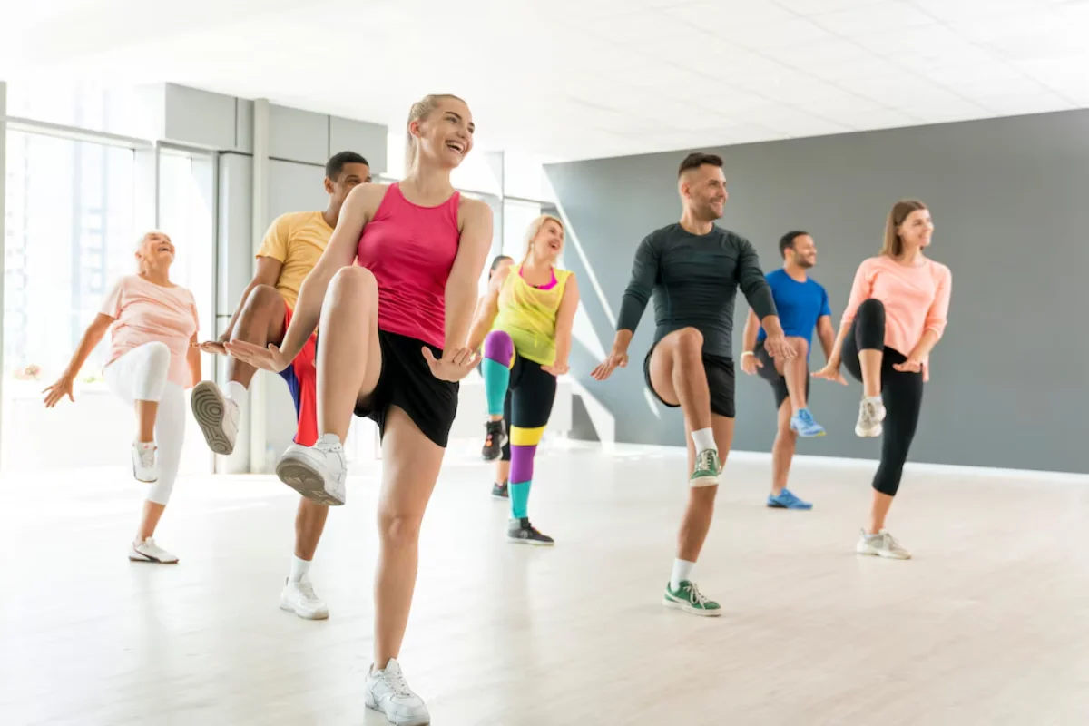 Diverse group of adults enjoying a high-energy dance fitness class in a bright, modern gym.