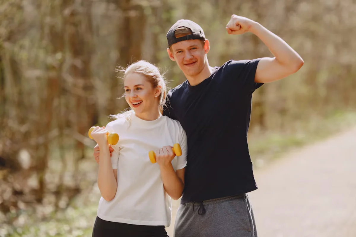 Two young adults jogging and exercising with hand weights in a sunny forest setting.