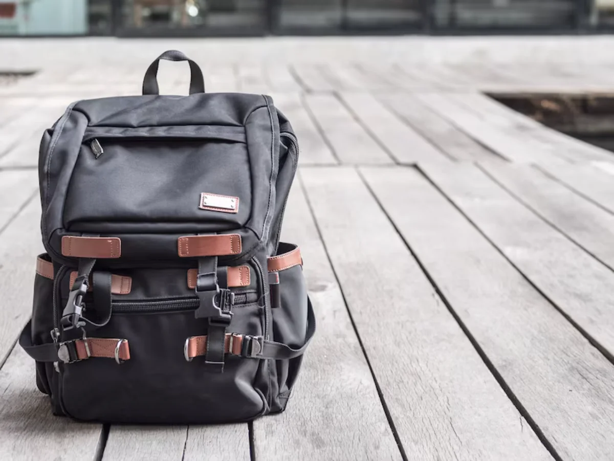 A black backpack with brown straps on a wooden boardwalk.