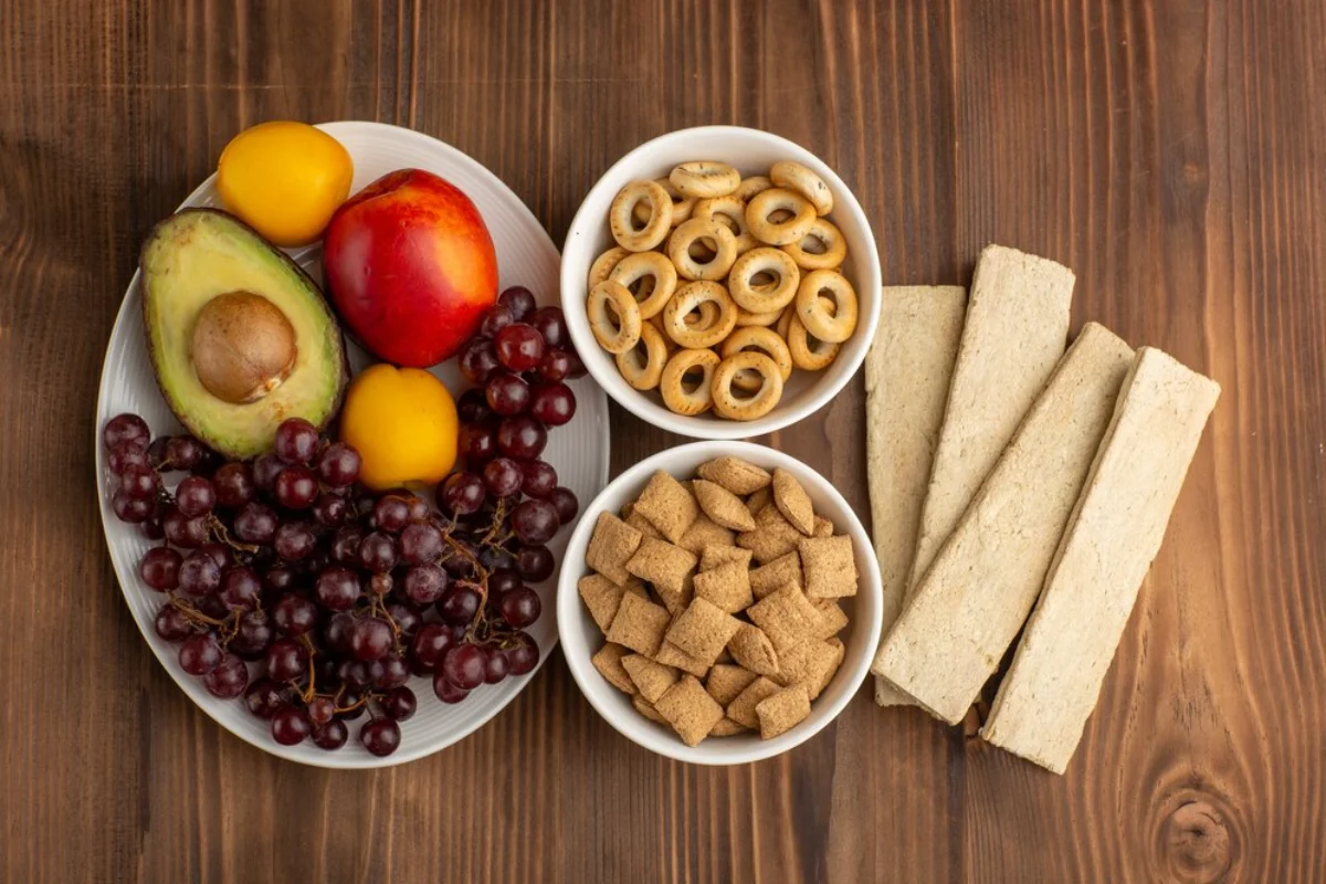 Various healthy snacks including fruits, cereals, and crackers on dishes against a wooden background.