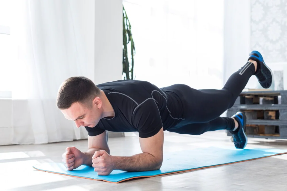 Man performing a plank exercise on a blue mat in a bright room.