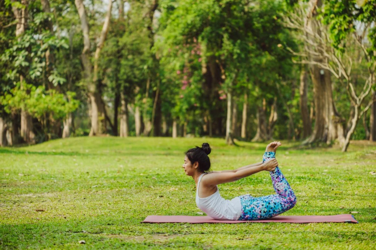Woman practicing yoga in a peaceful park, performing a stretching pose on a mat.