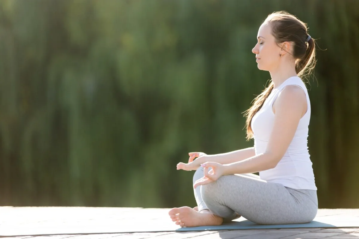 A woman meditating outdoors in a peaceful sitting position.