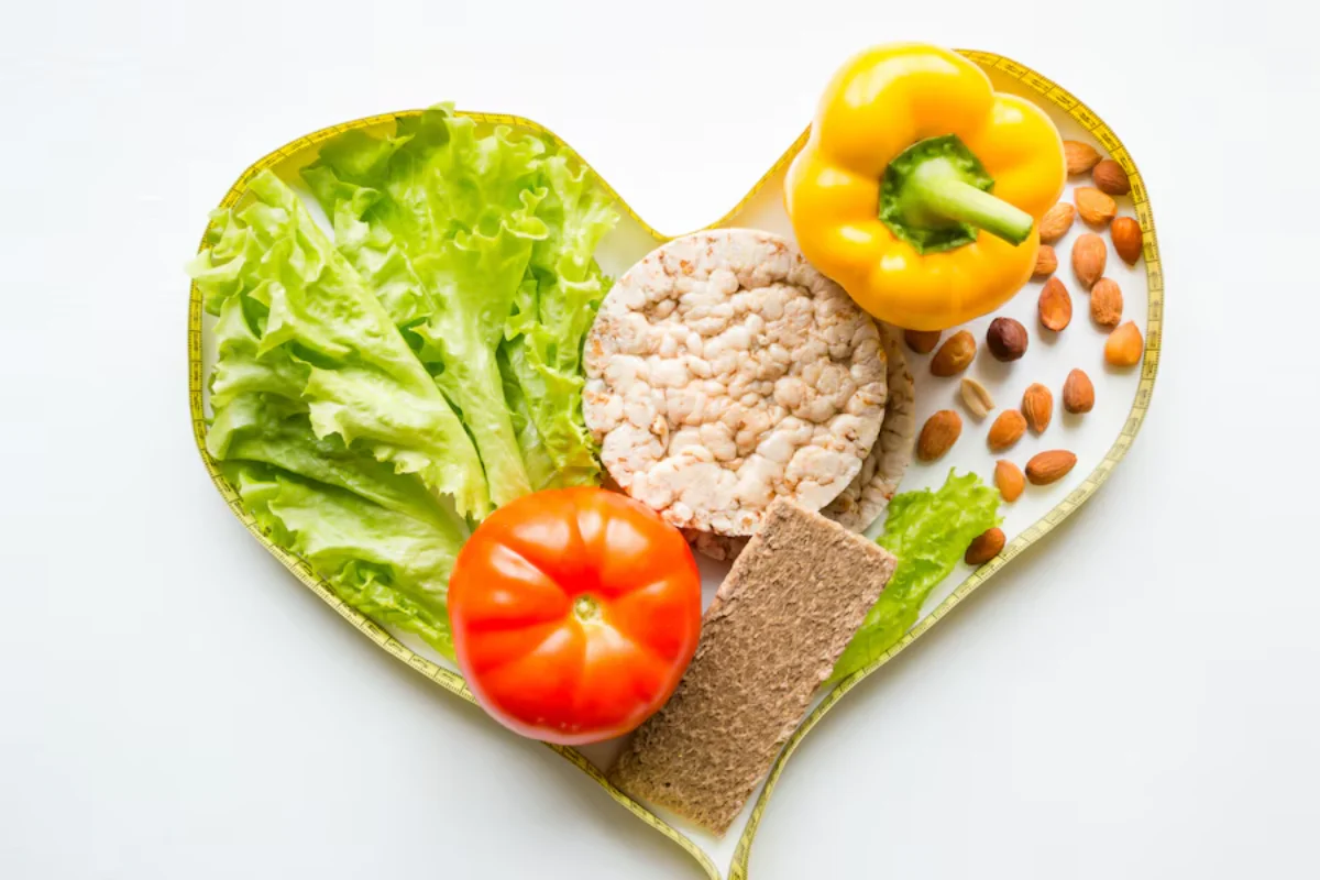 Heart-shaped plate filled with healthy foods including lettuce, tomato, bell pepper, nuts, and whole grain crackers.
