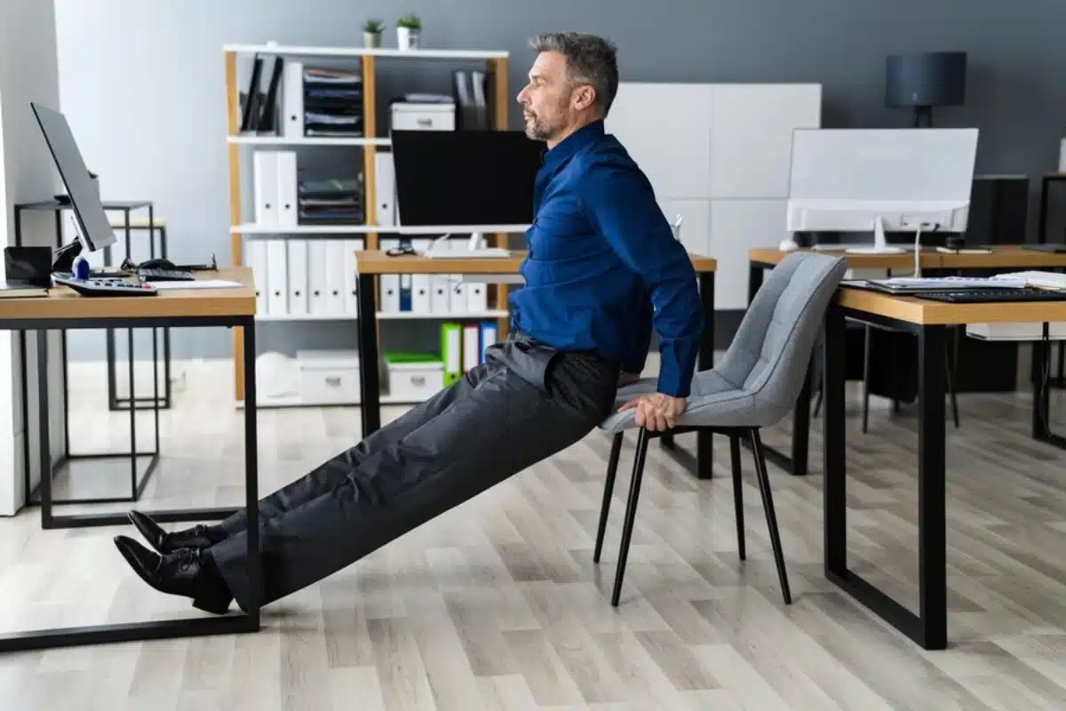 Man doing a tricep dip on a chair in a modern office setup.