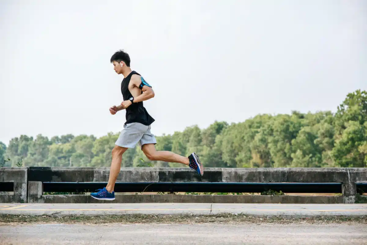 Young man running on a rural roadside in sportswear with trees in the background.