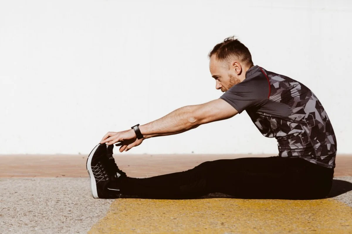 Man doing a seated leg stretch outdoors on a sunny day.