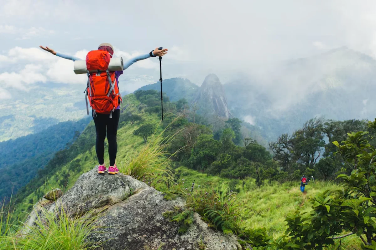 A hiker with arms outstretched stands on a mountain summit, overlooking a misty landscape.