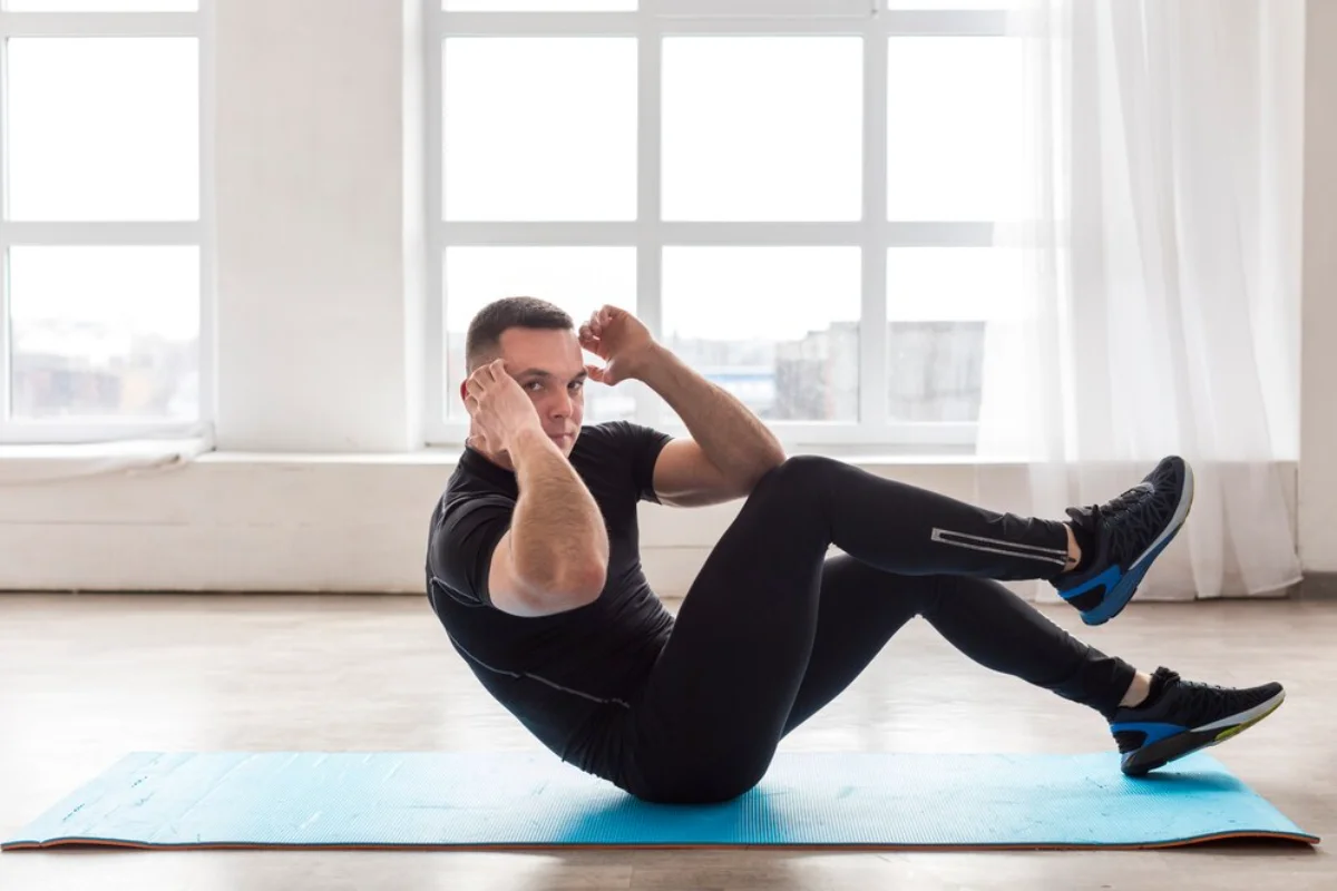 Man doing sit-up exercises on a blue mat in a bright room with large windows.