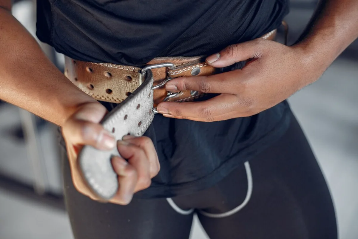 A person fastening a large, perforated weightlifting belt around their waist.