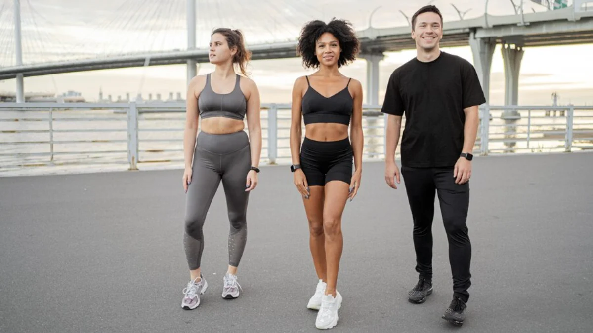 Three people in workout gear standing on a bridge, smiling and ready for exercise.