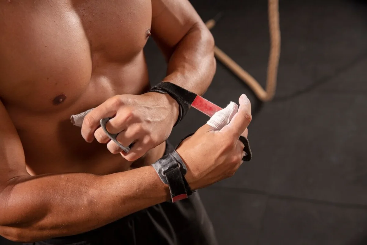 Close-up of a shirtless male athlete applying chalk to his hands in a gym.