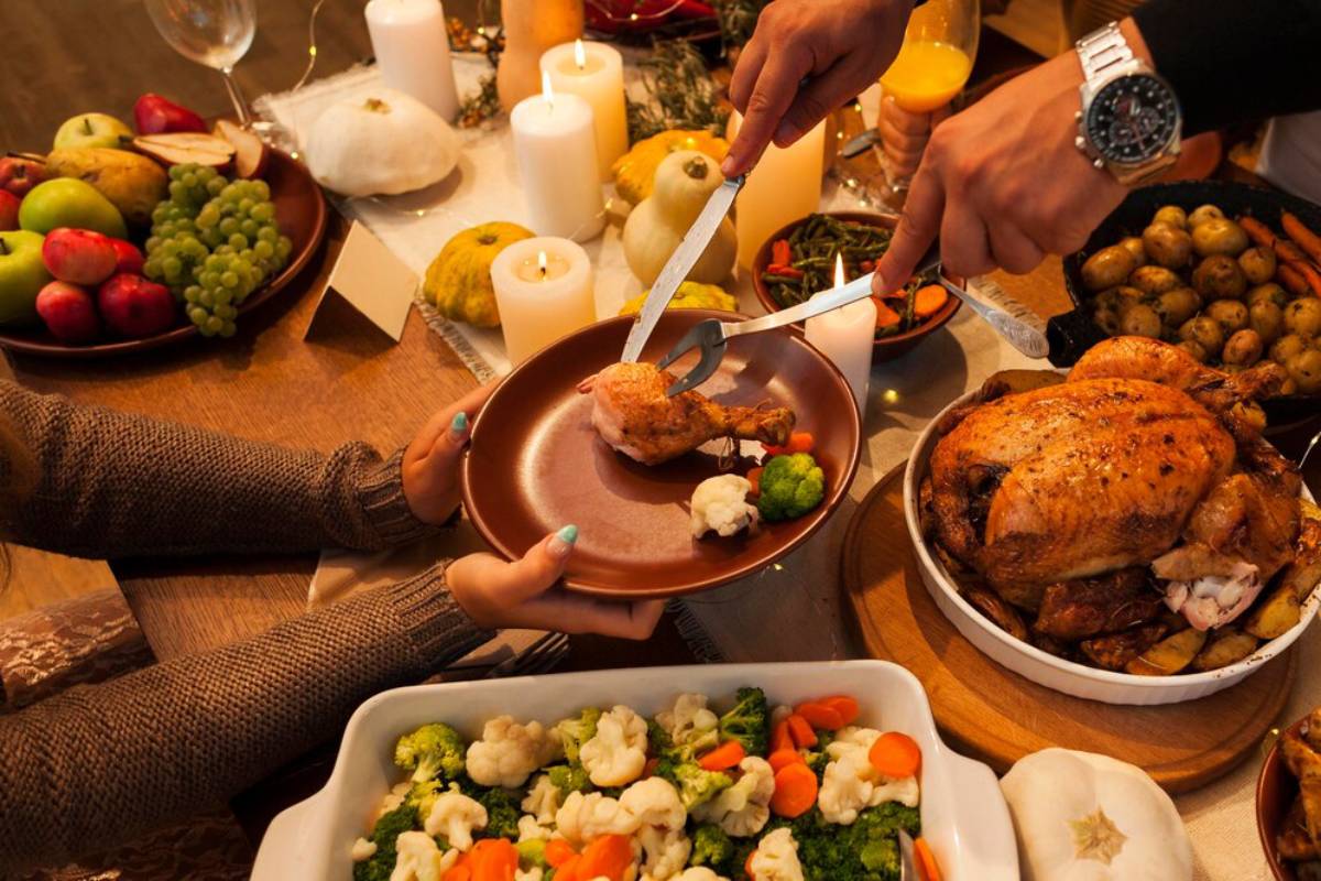 A festive dinner table with candles, fruits, and someone serving a turkey leg to a plate.