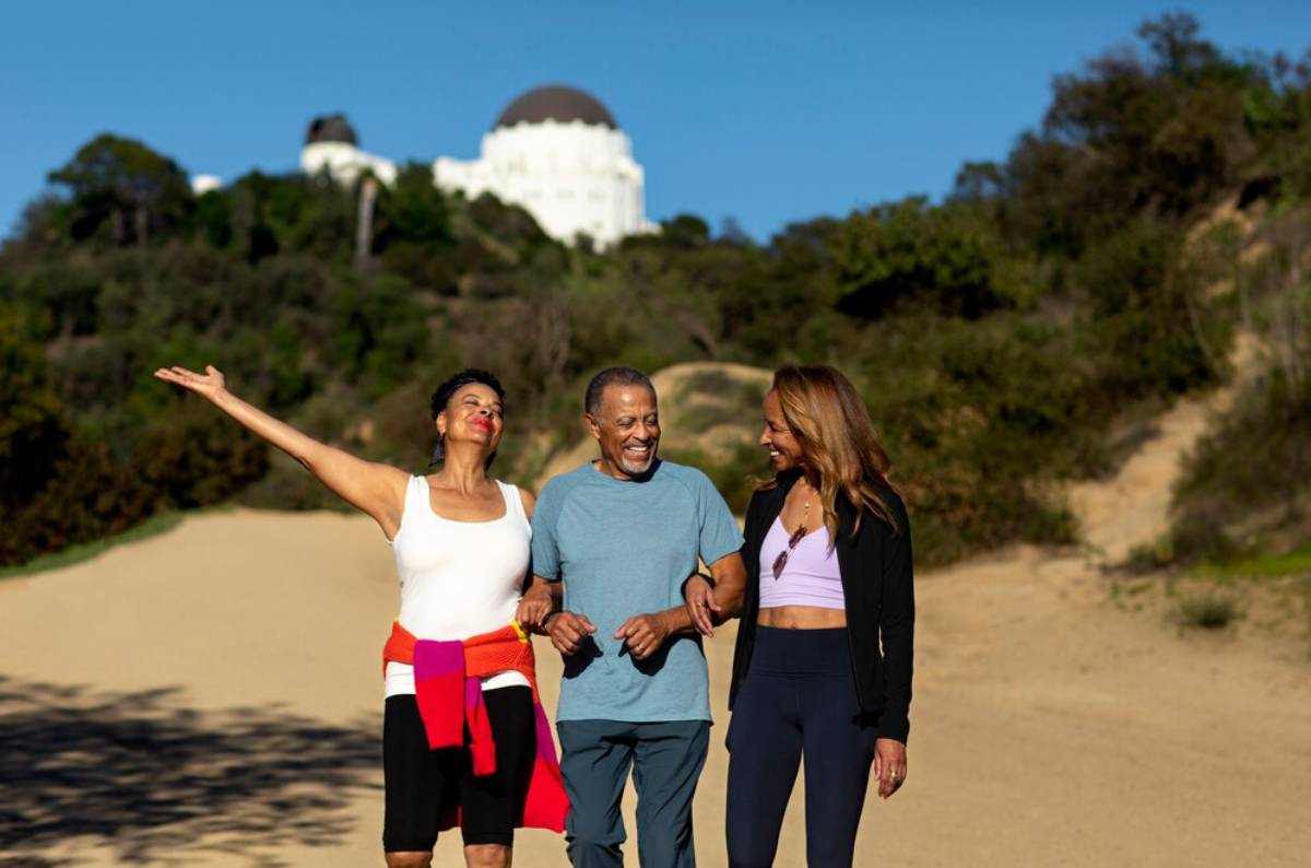 Three adults walking and laughing near a white-domed building on a sunny day.