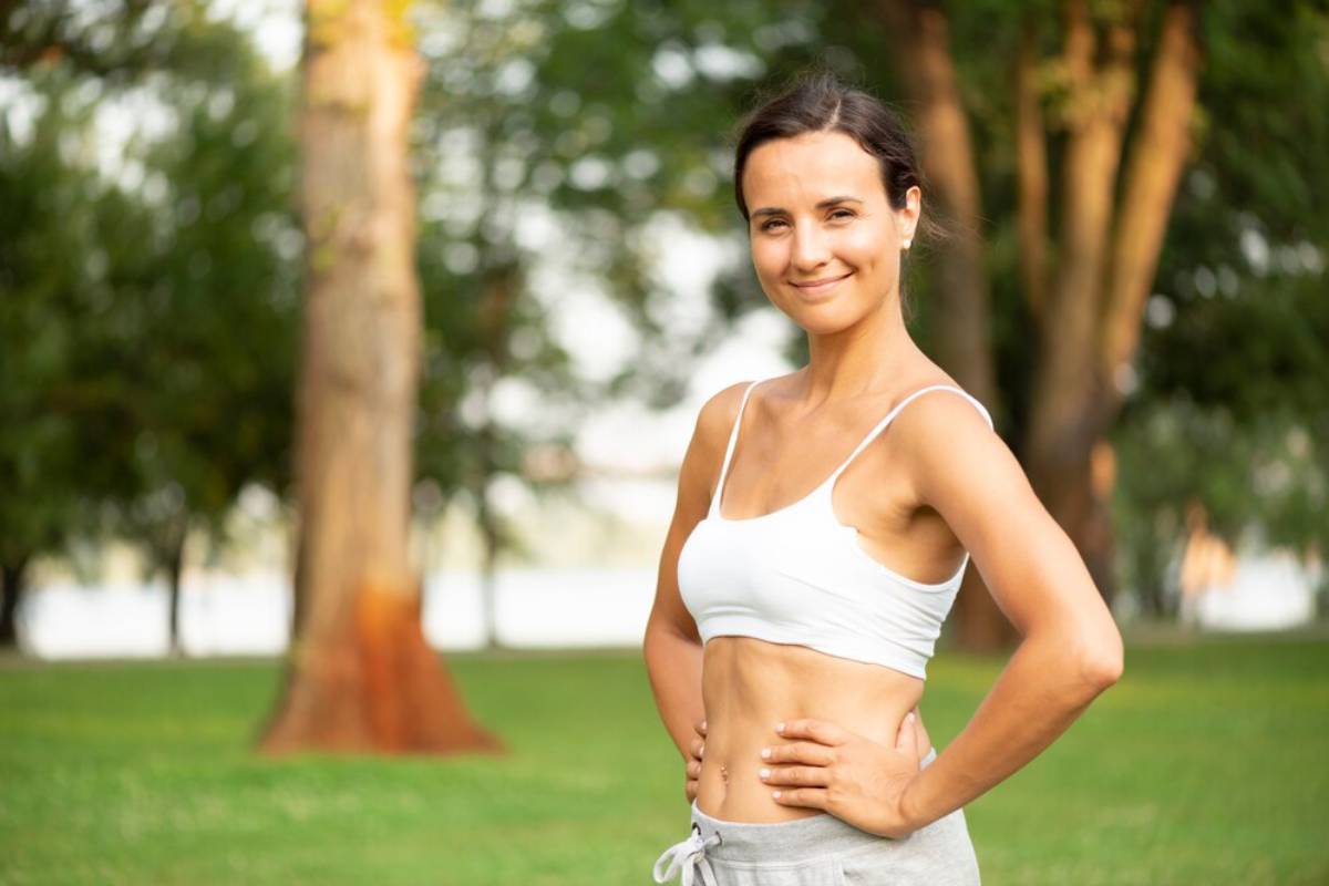 A woman in athletic wear smiling in a sunny park.