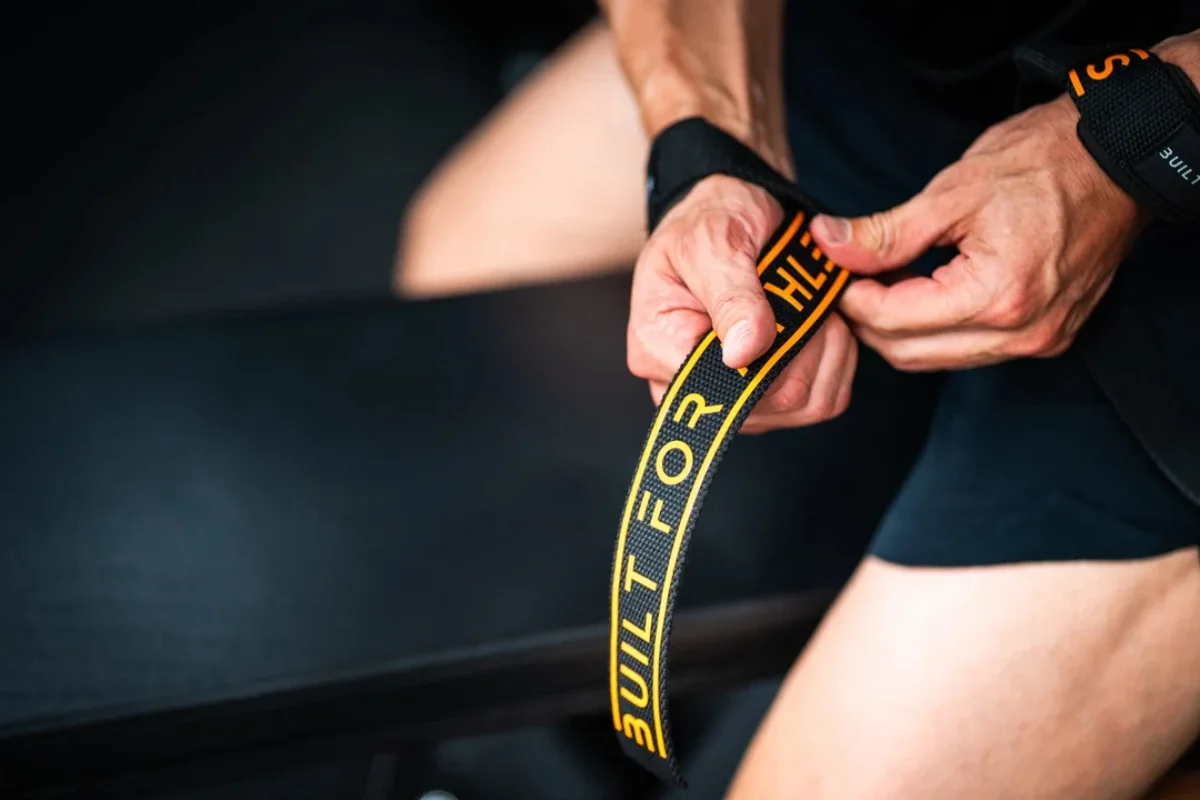 A person fastening a wrist strap with text BUILT FOR THE during a workout session.