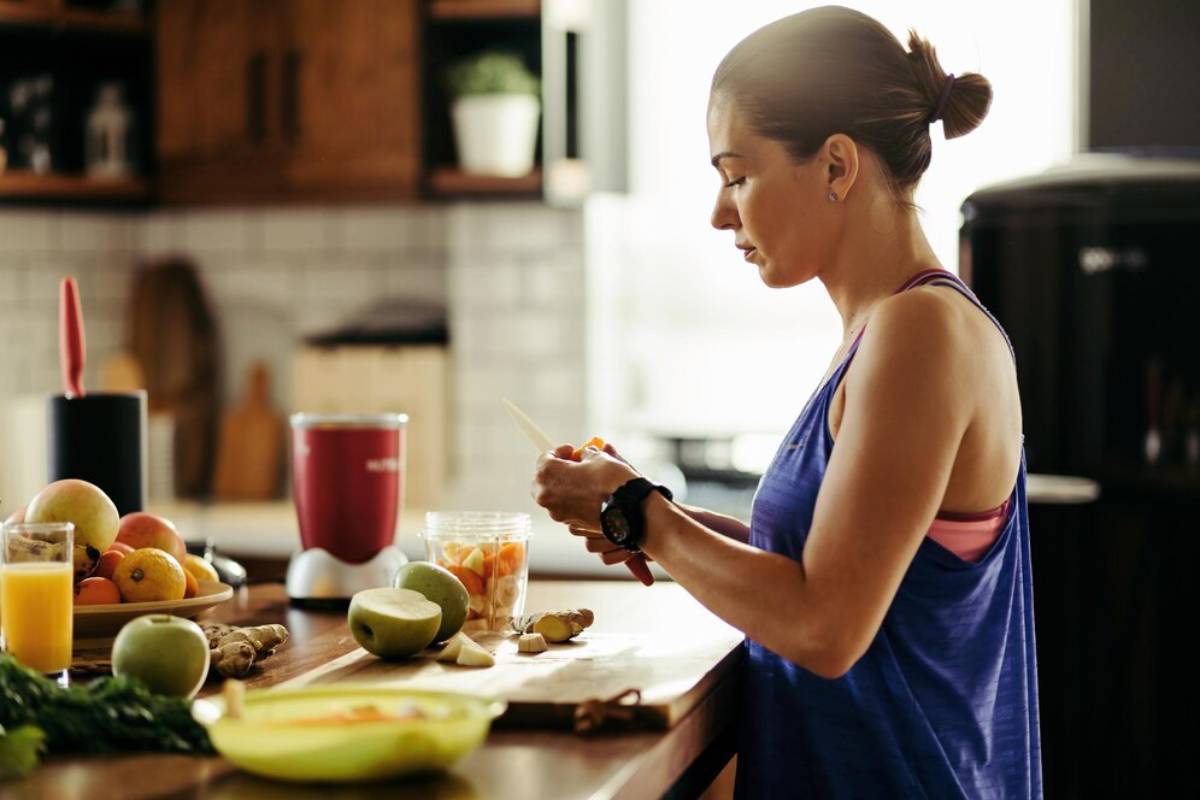Woman preparing food in a sunny kitchen with fresh fruits and vegetables on the counter.