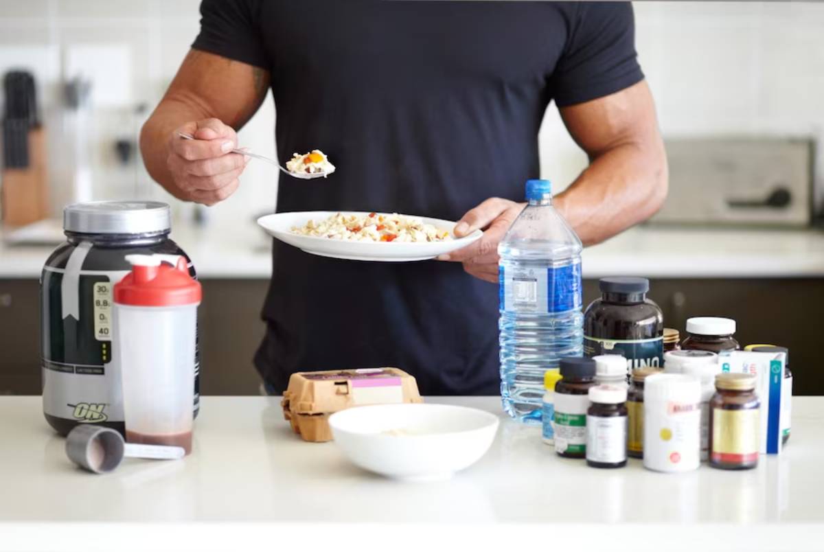 Man in a black t-shirt eating a healthy meal in a kitchen with dietary supplements and protein shake on countertop.