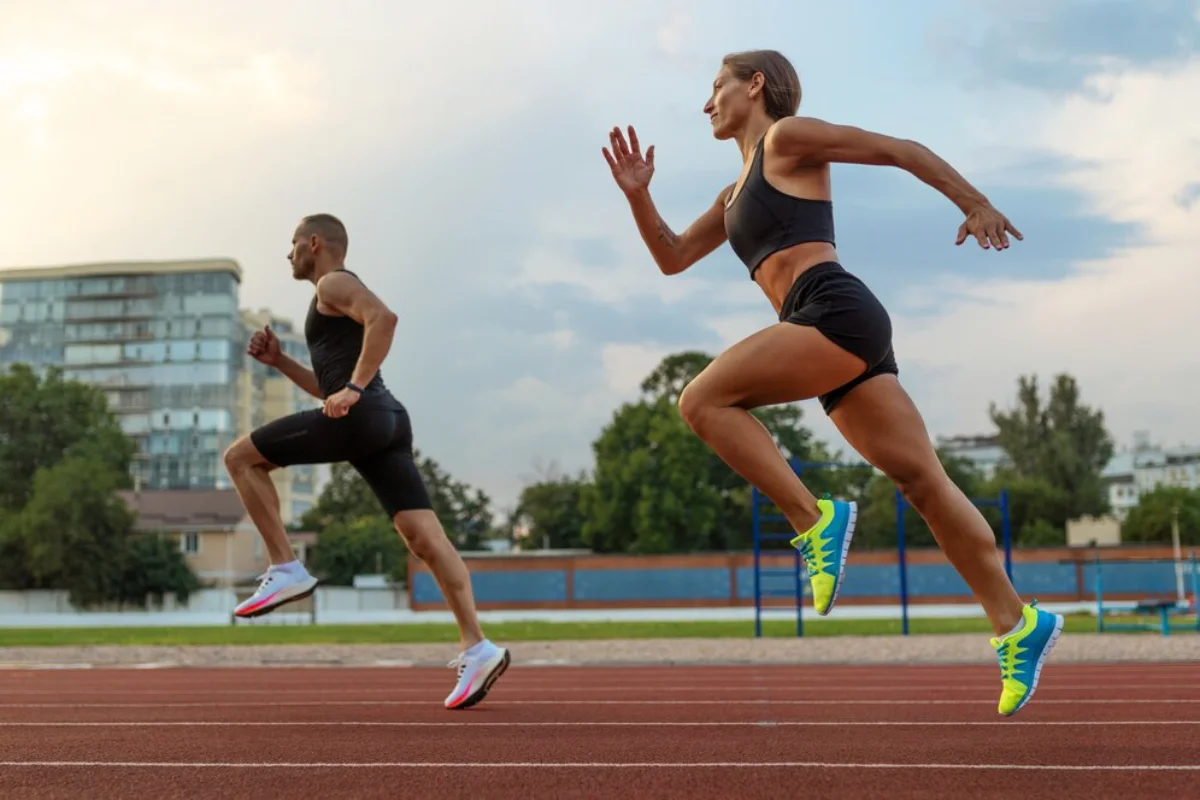 Two athletes sprinting on a track, with focus and determination, in an urban setting at dusk.